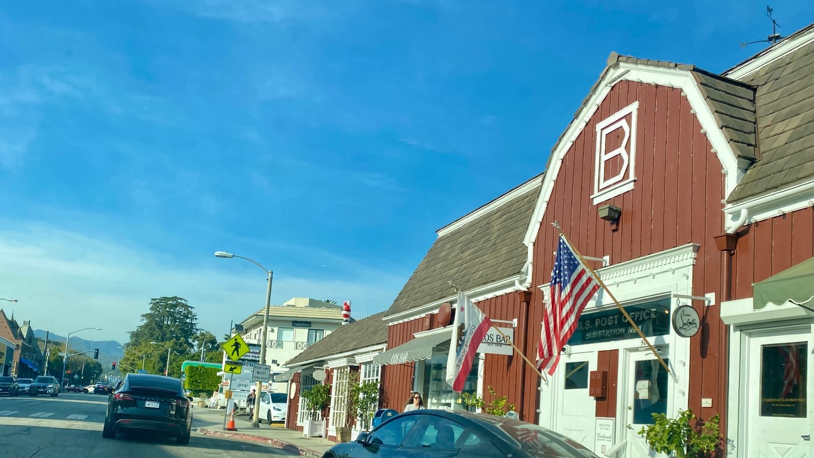 The red barn-style buildings of the Brentwood Country Mart with an American flag, beside 26th Street