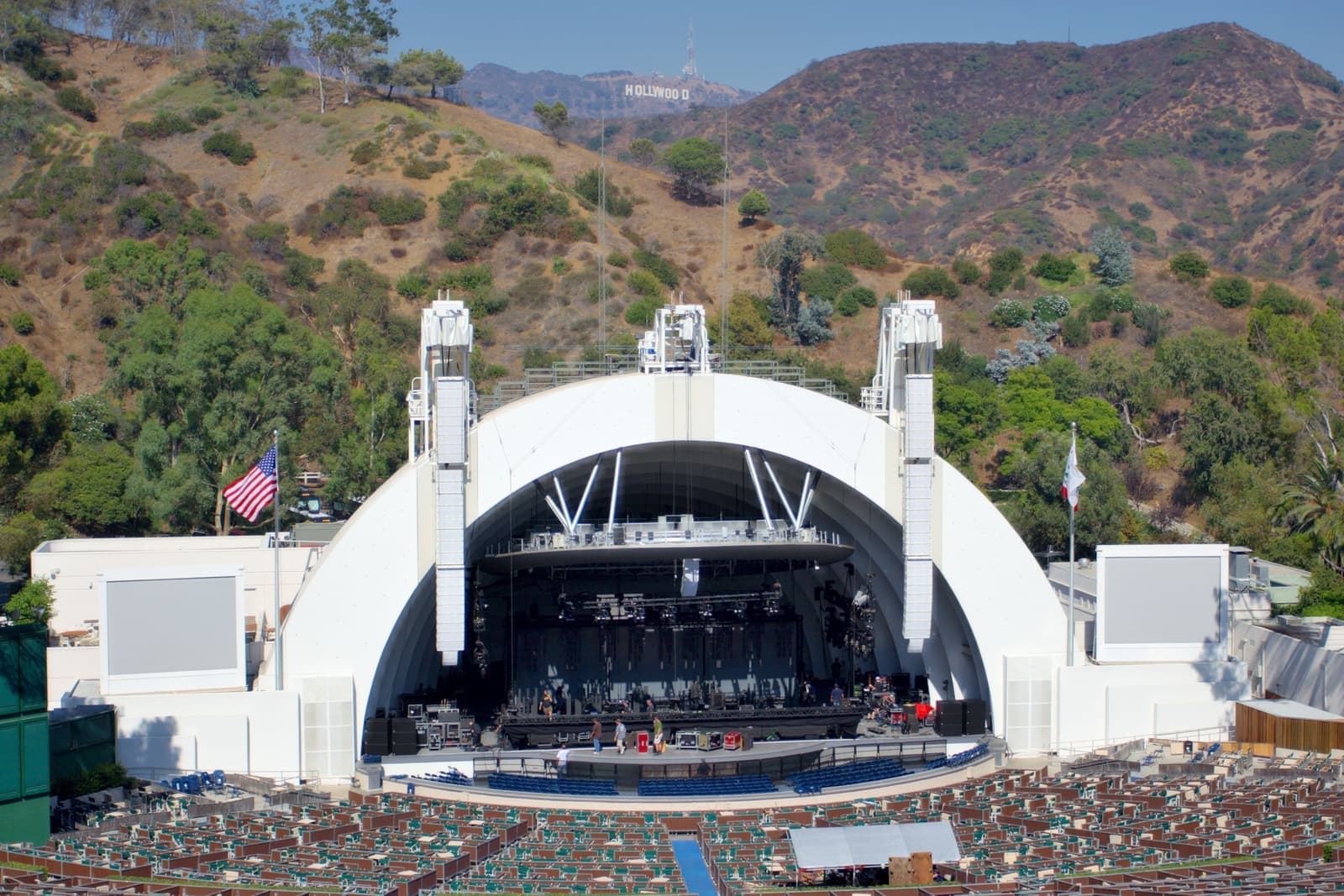 The white arched shell of the Hollywood Bowl and its empty seats, with brushy green hills and the Hollywood Sign on the ridge behind