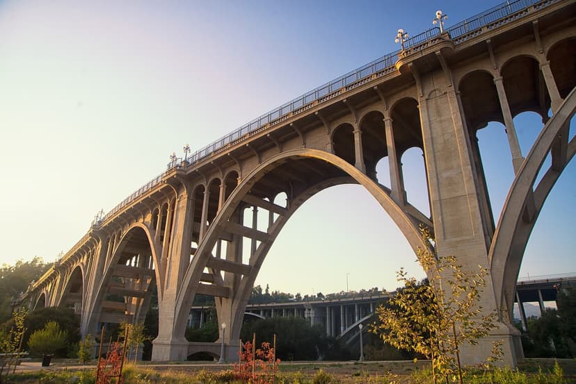 The concrete arches of the Colorado Street Bridge lit by the setting sun, seen from the park below