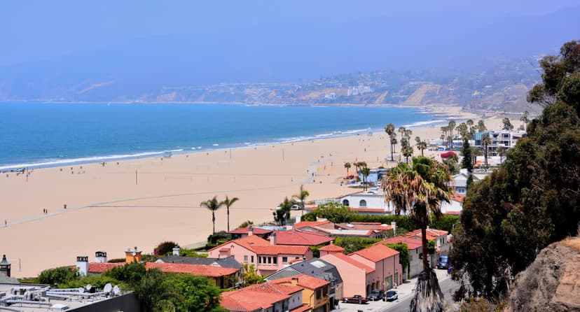 View from the Palisades Park bluff over the beach, red-tile roofs along PCH and the Malibu coast