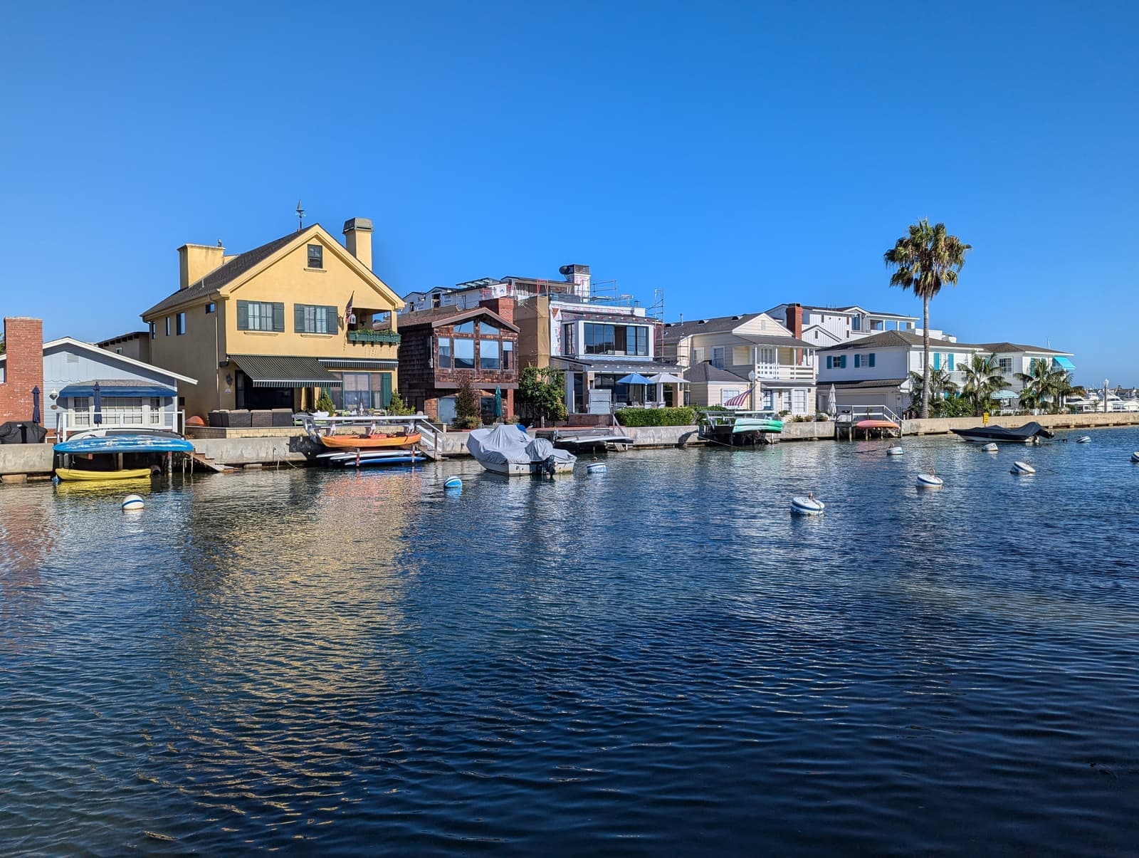 A yellow two-story house and neighboring homes with docks line the Grand Canal, small boats on calm blue water under a clear sky