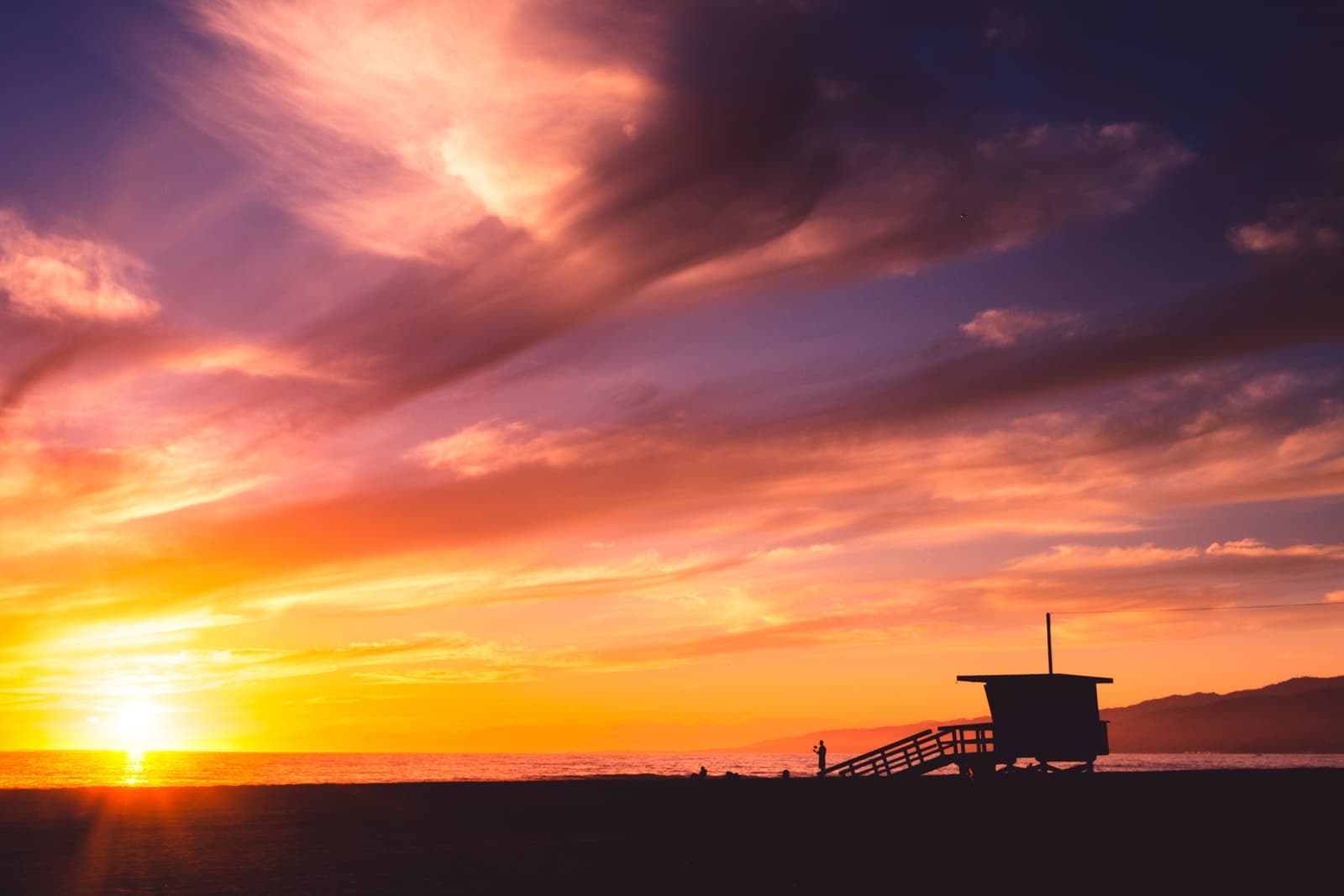 Pink and orange sunset clouds over the ocean with a lifeguard tower in silhouette