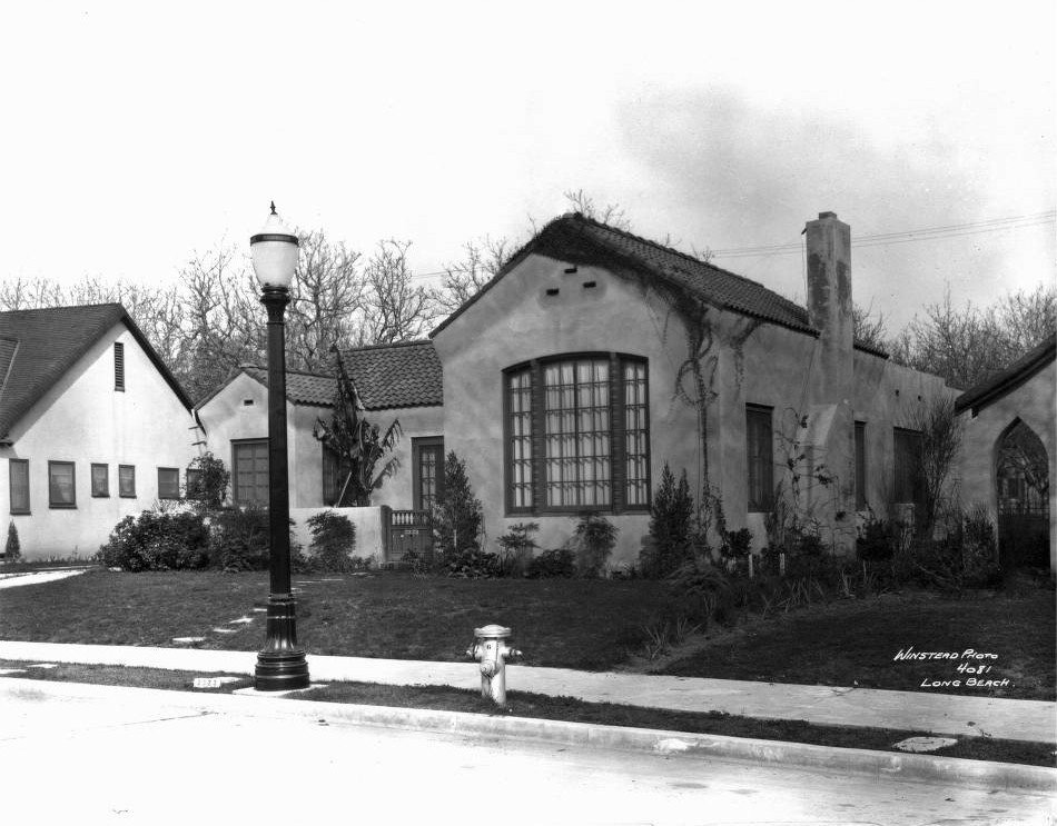 A 1920s Spanish Colonial Revival bungalow with tile roof, arched window, and a vintage streetlamp in California Heights, Long Beach